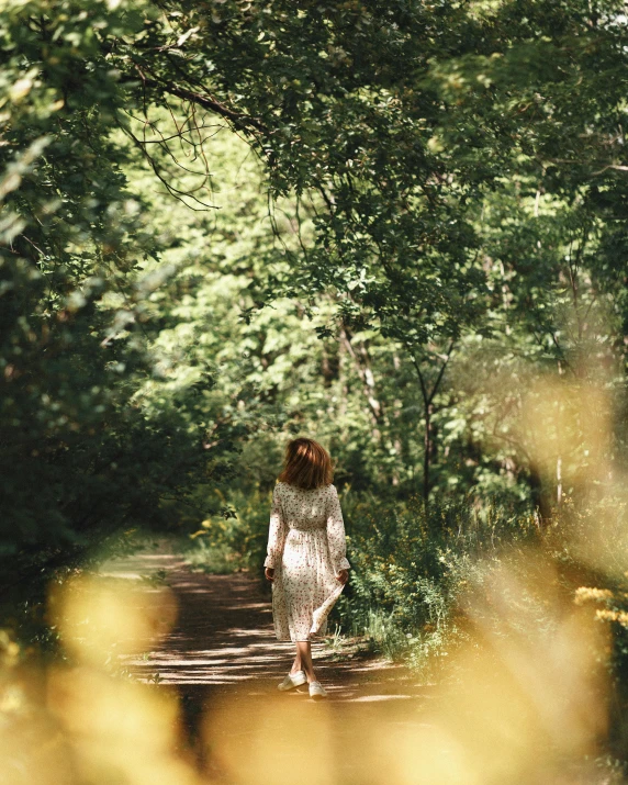 a woman walking down a dirt road surrounded by trees