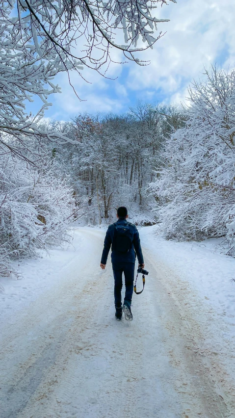 a man walking along a snowy road with a snowboard