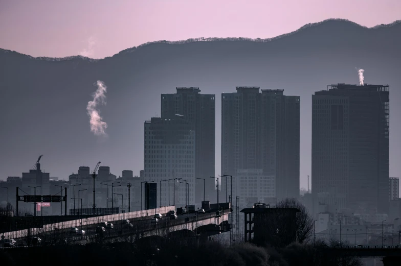 a city with mountains in the background and smoke coming out from the stacks