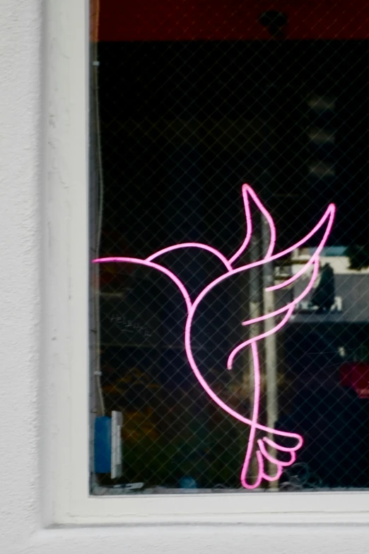 pink neon humming bird sitting outside a window