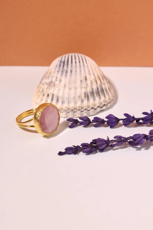 two rings, one with an ayst, and the other with lavender, lie on a counter with a shell