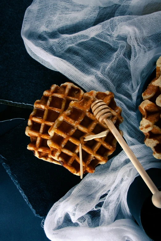 a honeybee waffle on a cloth next to a cup of syrup