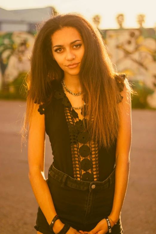 an attractive young woman wearing overalls poses in front of graffiti covered walls