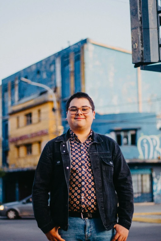 a man in glasses and jacket posing on street corner near building