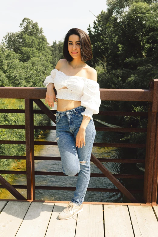 a beautiful woman posing on a bridge wearing jeans and a white top