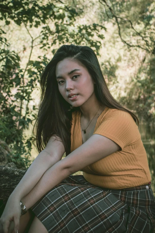 a woman wearing a yellow shirt and a plaid skirt sitting on a tree nch