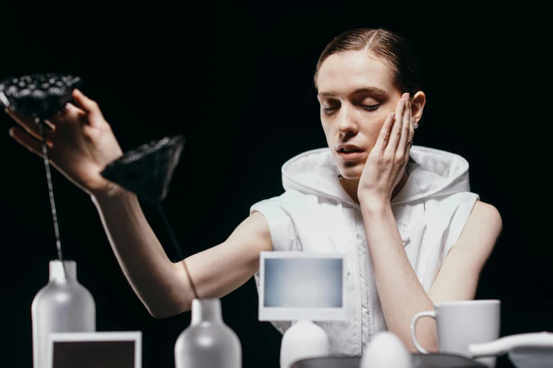 a woman covers her face with her hand as she sits by table of alcohol bottles