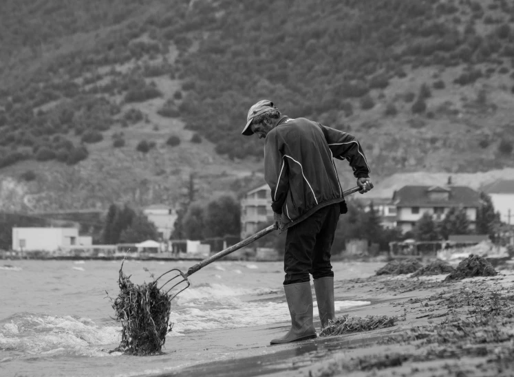 black and white po of man with shovel digging on beach