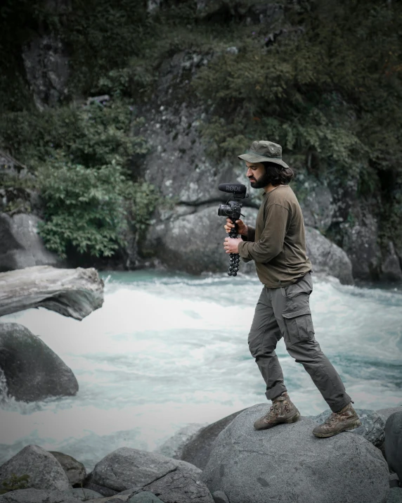 a man standing on rocks by a stream and holding a camera