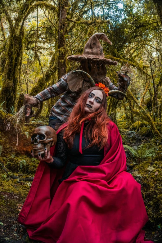 a woman is dressed in a red costume while a scarecrow in costume is holding a dead doll