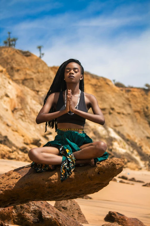 young woman with black hair wearing african clothing sitting on large rock