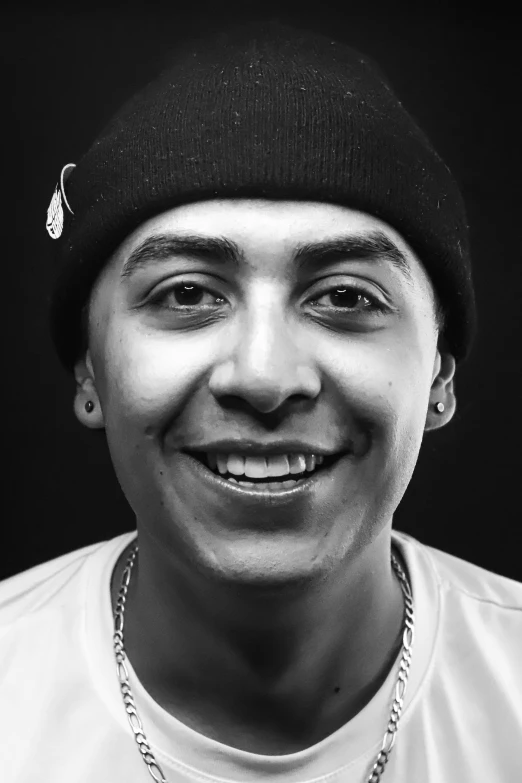 black and white image of smiling male with necklace and beanie