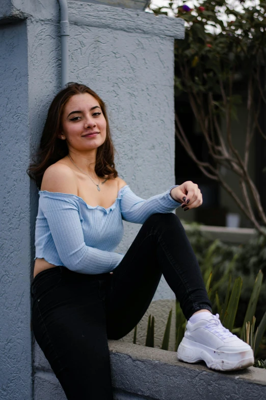 a woman posing while wearing white sneakers and blue sweater