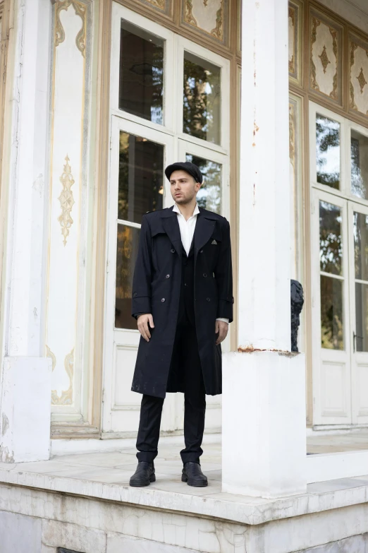 a young man wearing a hat stands in front of the entrance of an old building