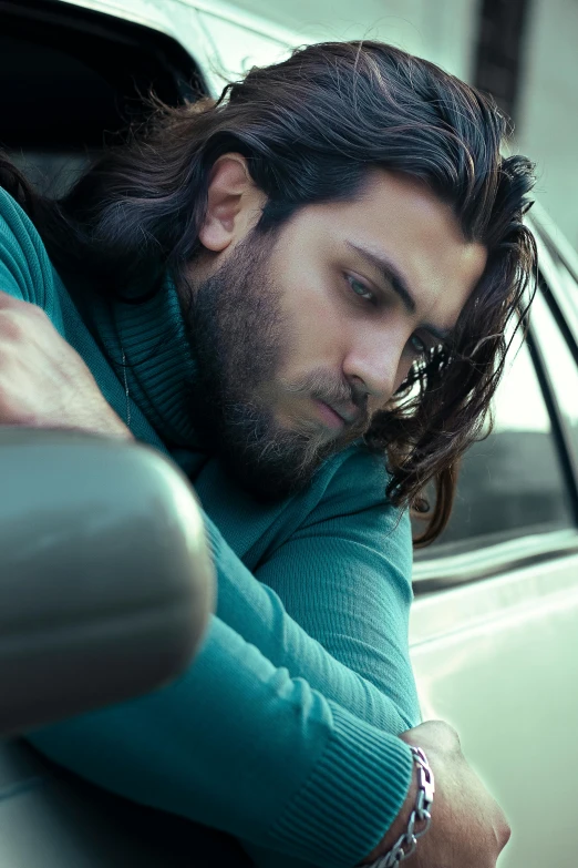 a man with long hair leaning on the passenger side of a car