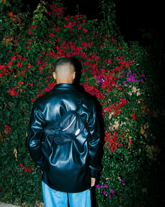 a man in a black leather jacket standing next to a plant