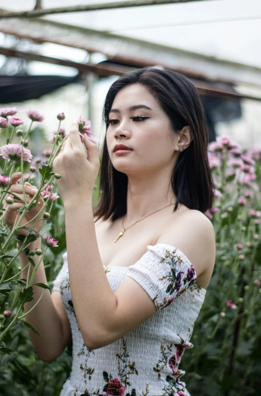 an attractive woman in a white dress smelling some purple flowers