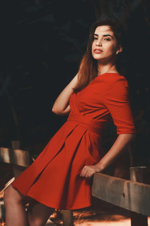 a woman in a red dress leaning on a fence