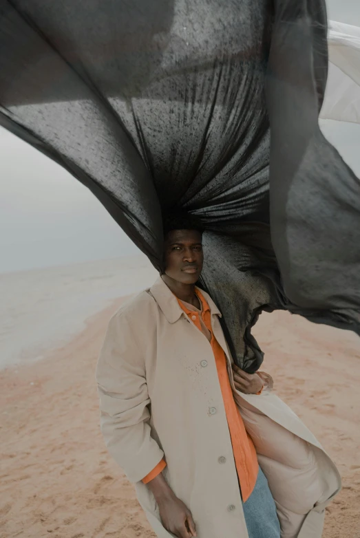 man standing in sand holding his coat and looking at camera