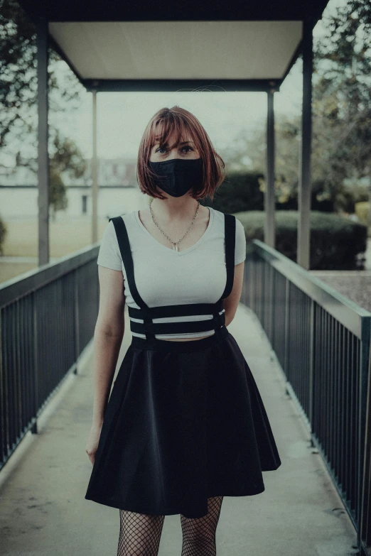 a woman wearing a black mask and suspenders stands on a bridge