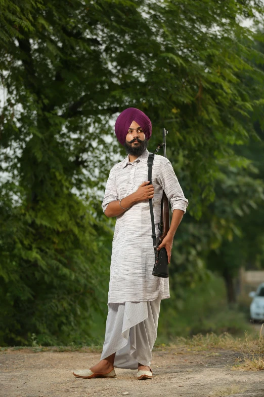 an indian man holding a rifle in front of a forest