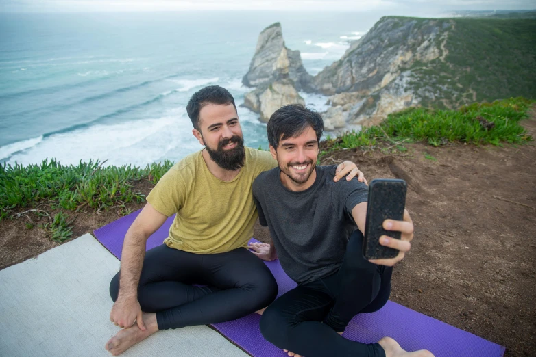 two people sitting on top of a purple mat holding up a cell phone