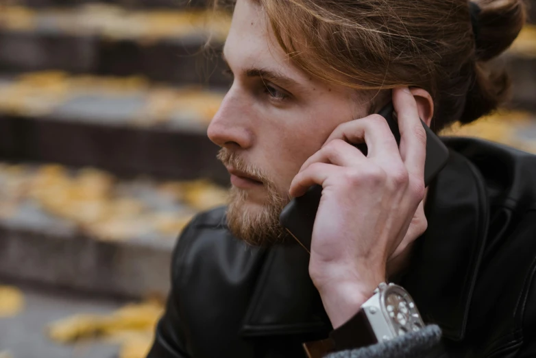 a young man with a beard and leather jacket is talking on the phone