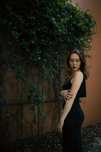 a woman wearing a black dress standing next to a bush