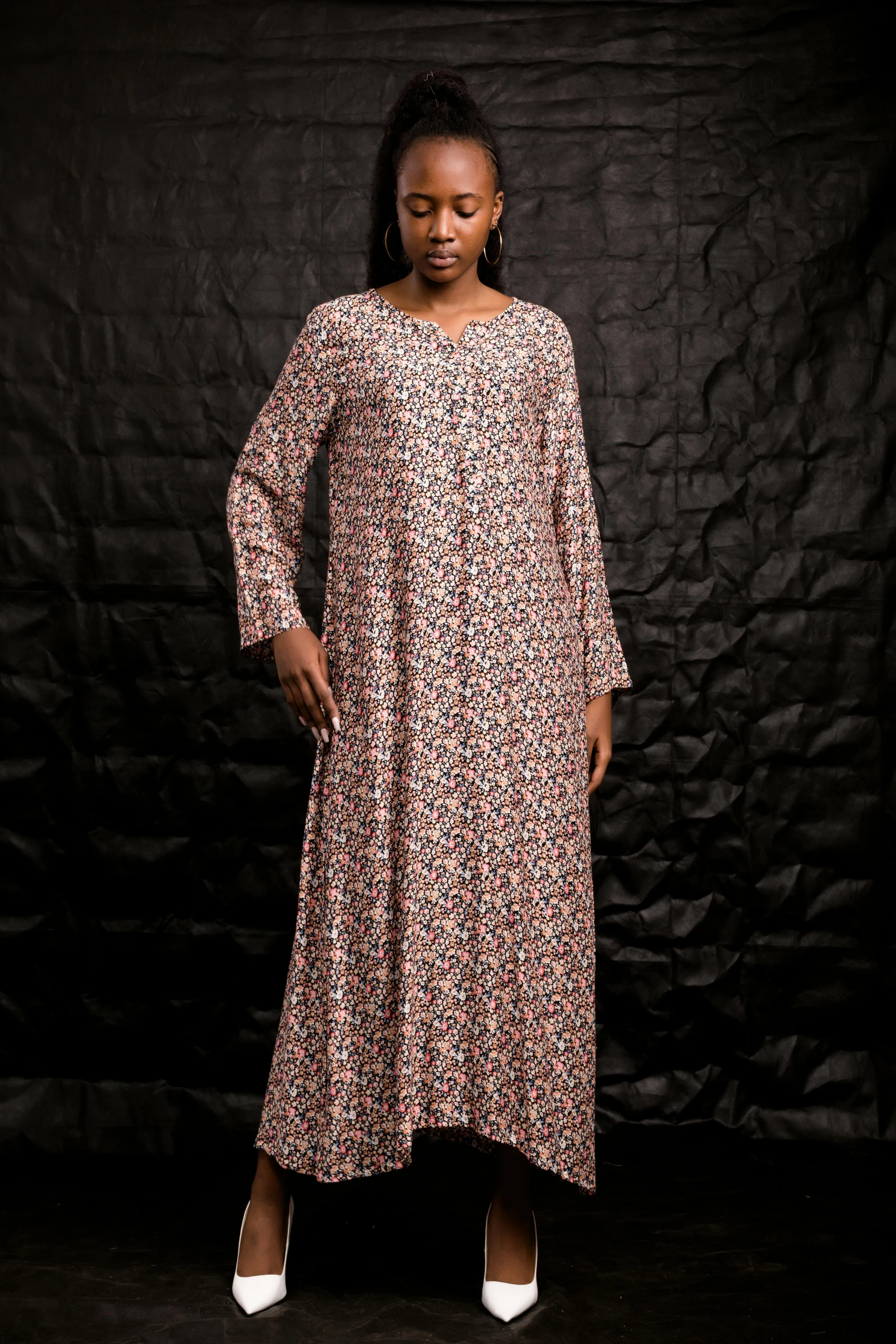 a woman standing in front of a black backdrop wearing a dress