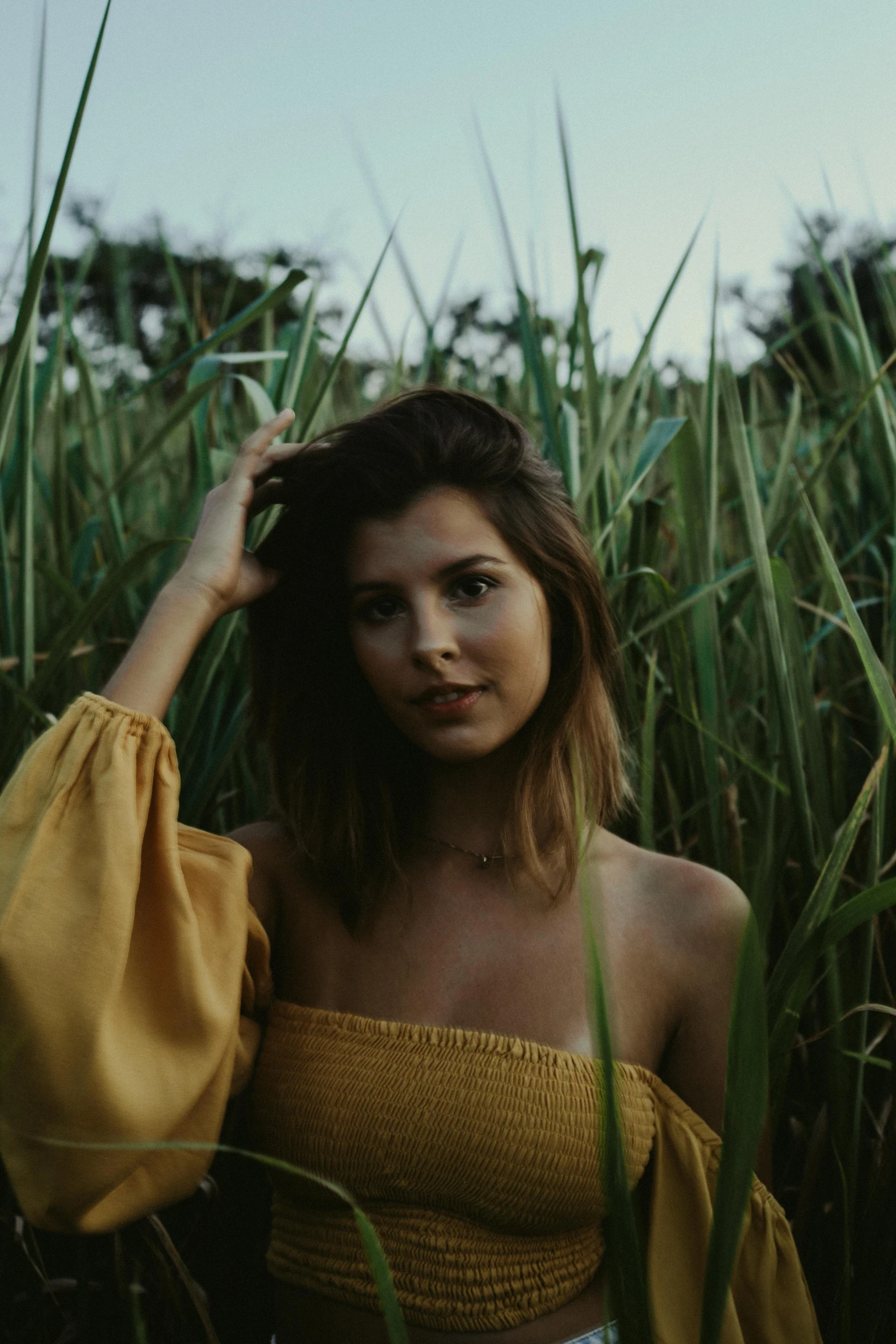 an attractive woman standing in tall grass with her hand on her hair