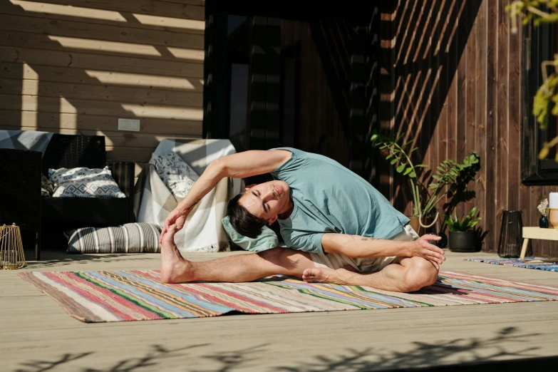 a man doing yoga on top of a rug on a deck