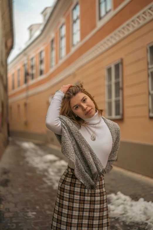 the woman poses with her hands behind her head in a plaid skirt