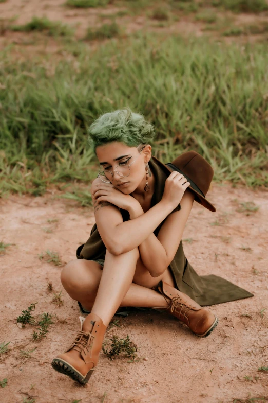 a woman with green hair and glasses sitting on the ground