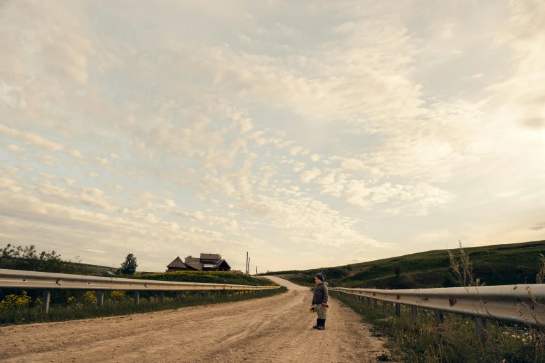 a man walking down a dirt road while the sun goes down