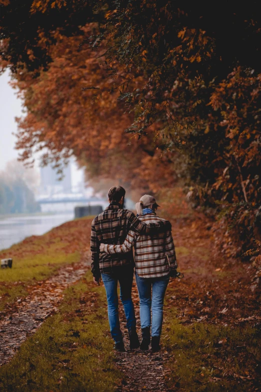 two people walking along a path by the water in the fall