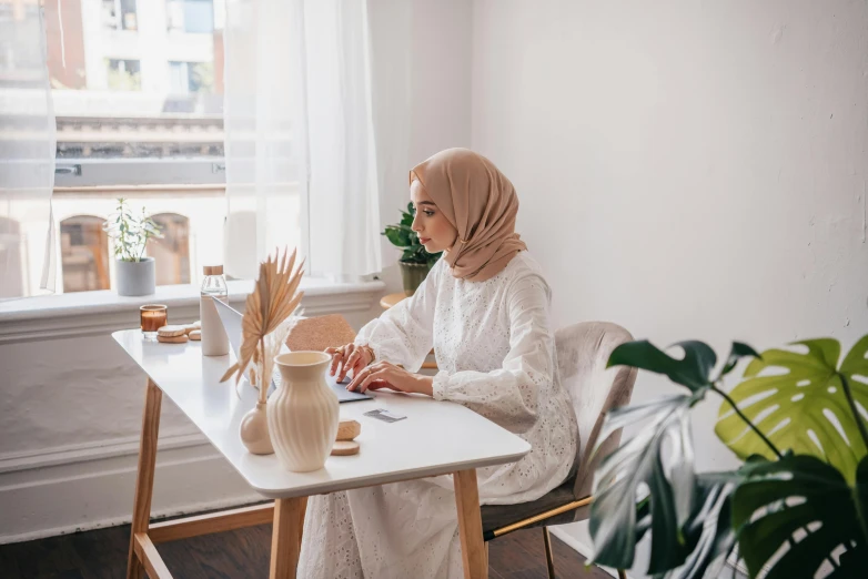 a woman wearing a headscarf sitting at a desk with her computer