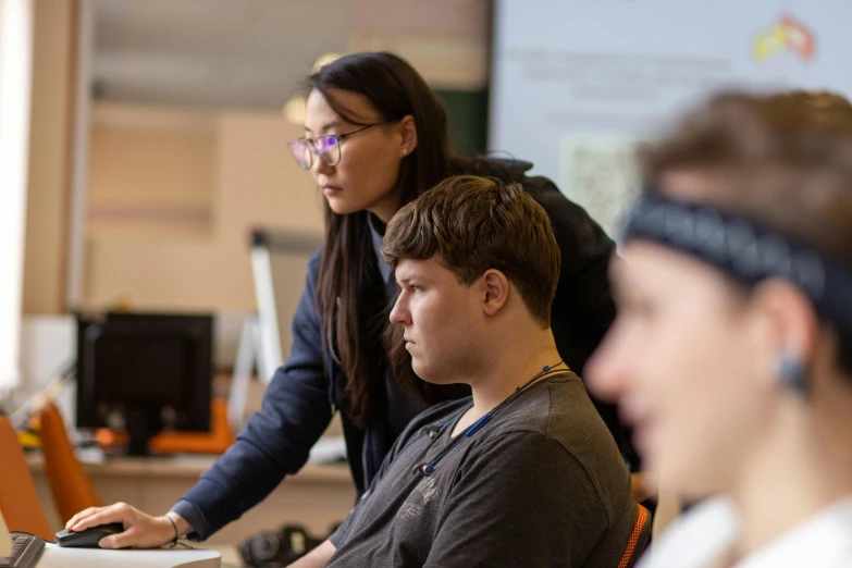 two students are working on computers while another student looks at them