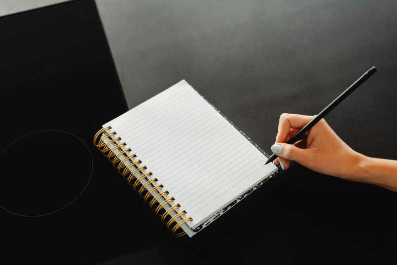 a person writing on a note book with pencil