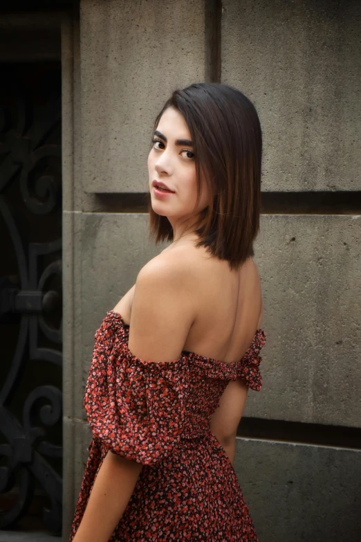 young woman standing next to stone wall in dress