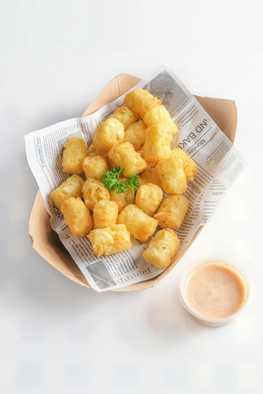 a bowl of fried food on a newspaper and some sauce