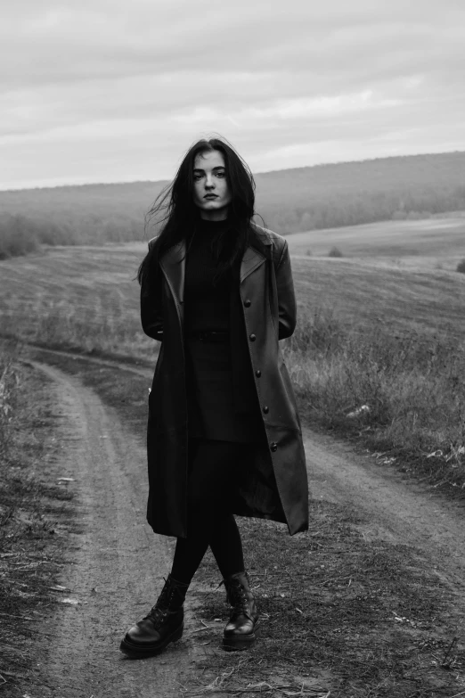 a woman walking across a dirt road near a field