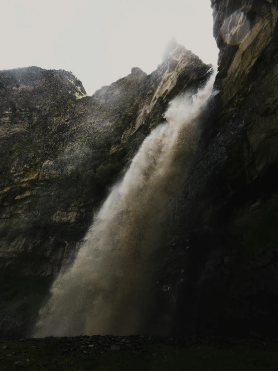 a tall waterfall spewing water into the air near a large rock cliff