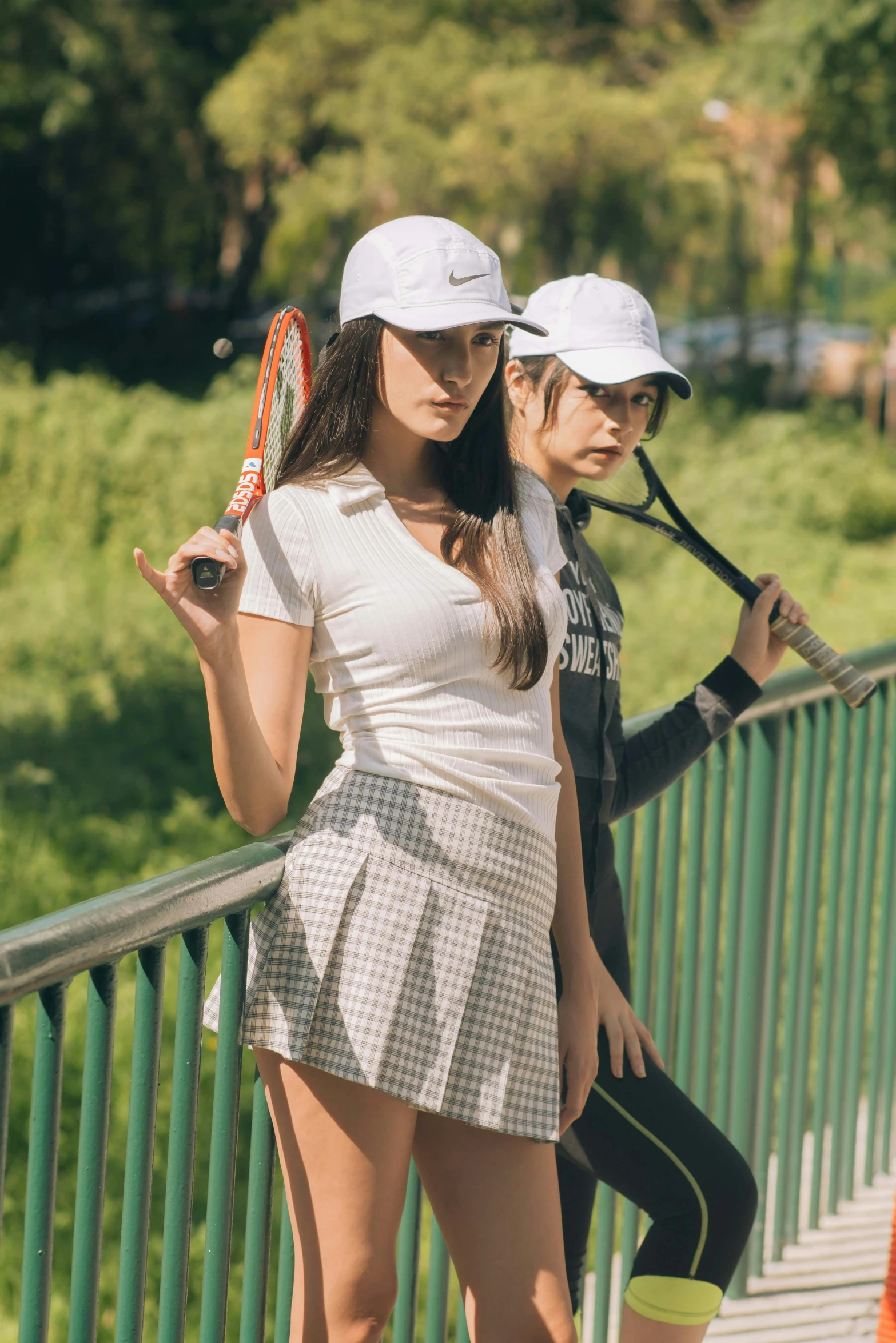 two young woman with tennis racquets pose on a bridge