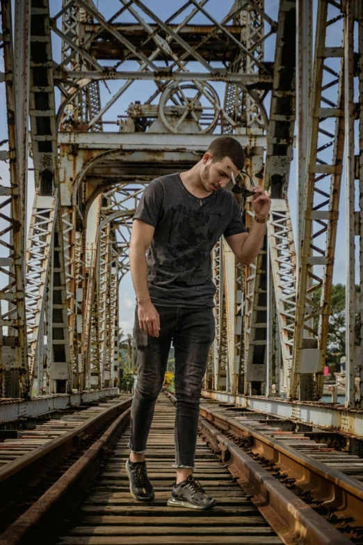 a person with his hand in his mouth standing on a rail road bridge