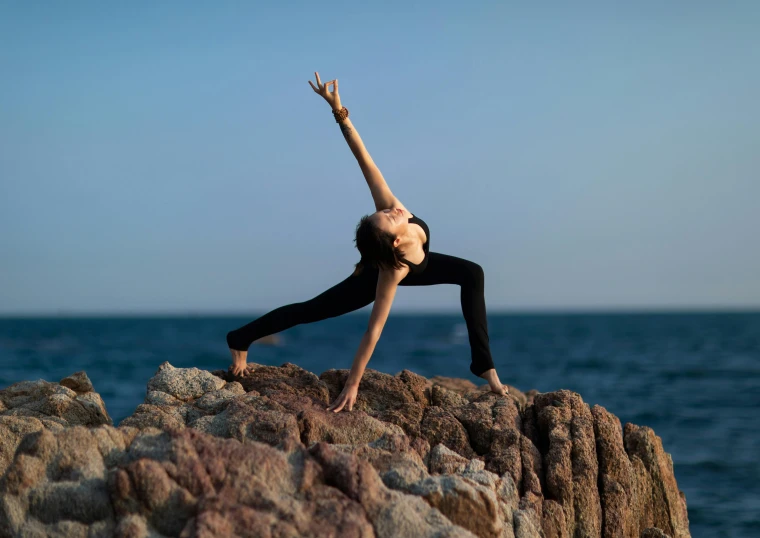 a woman practices yoga on the beach rocks