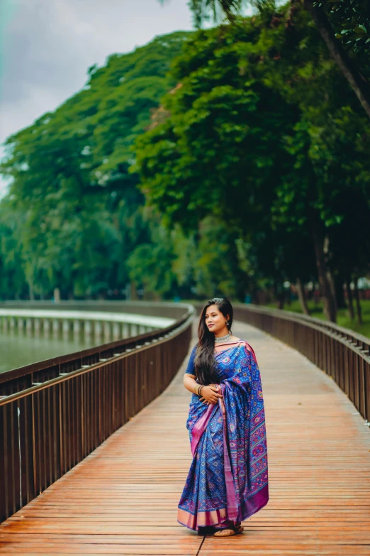 an indian woman standing on a wooden path in front of water