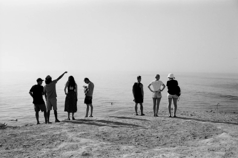 group of people standing around the beach pointing out to the ocean