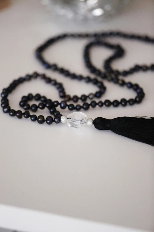 a necklace of beads and black tassel on a white table