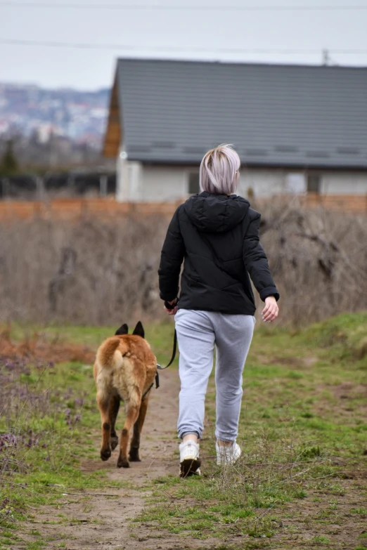 woman and dog walking on pathway in rural area