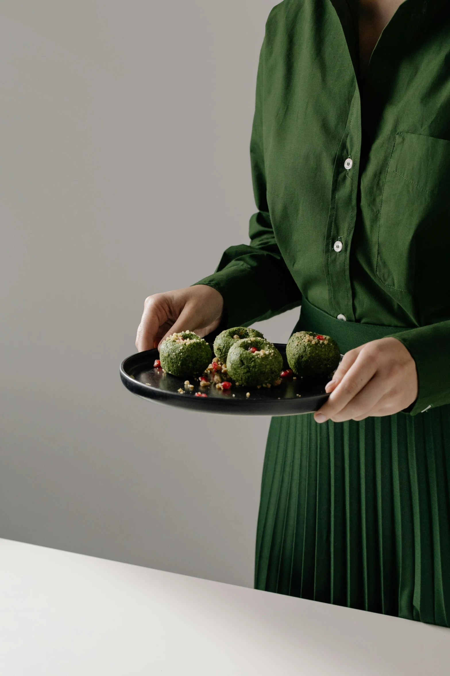 a woman holds a plate full of green desserts